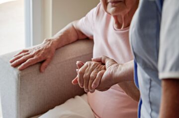 Pflegehelfer hält die Hand einer älteren Person