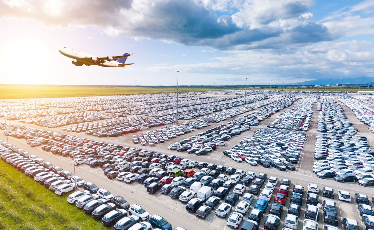 Weitläufiger Parkplatz am Flughafen Nürnberg mit zahlreichen Autos und einem startenden Flugzeug im Hintergrund.